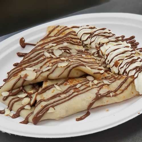A plate of crepes drizzled with chocolate sauce, topped with whipped cream and sliced almonds.