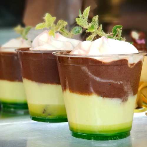Three layered dessert cups with green, yellow, and brown mousse topped with whipped cream and mint leaves.