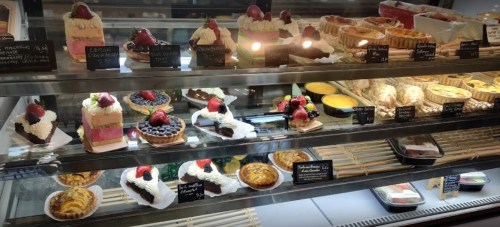 A display case filled with various colorful desserts, including cakes, tarts, and pastries, topped with fruits.