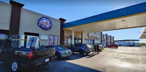 A pizza restaurant storefront with parked cars and a delivery truck in a shopping plaza.