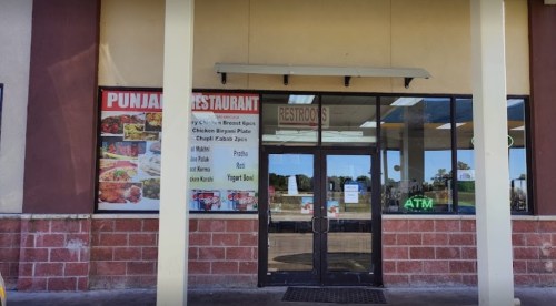 Entrance of a Punjabi restaurant featuring a menu display and restrooms sign, with an ATM visible nearby.