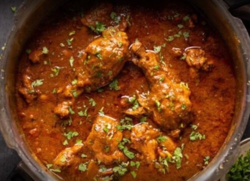 A pot of chicken curry garnished with fresh cilantro, simmering in a rich, spicy sauce.