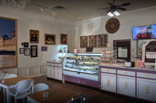 Cozy café interior featuring a display case of desserts, wooden tables, and elegant decor with artwork on the walls.