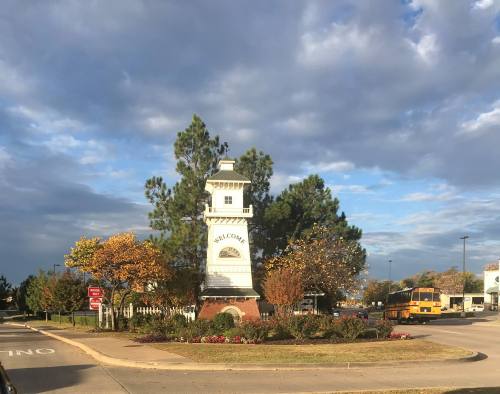 A welcome tower surrounded by trees and autumn foliage under a cloudy sky, located at a roundabout.