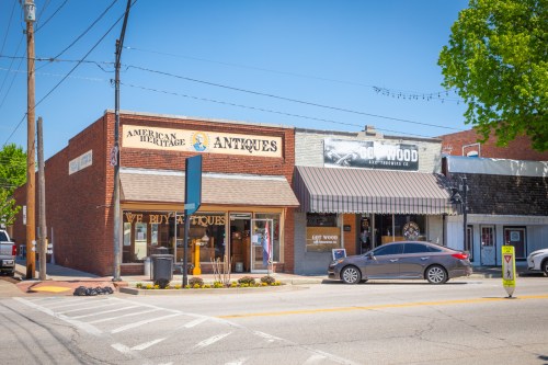 A street view of antique shops with brick facades and a parked car, under a clear blue sky.