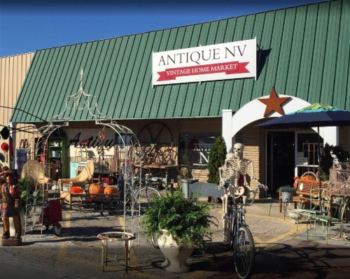 A vintage home market with a green roof, outdoor decor, and a skeleton on a bicycle in front of the store.