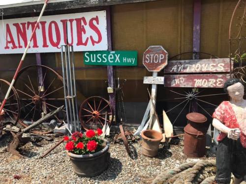 A collection of antique items, including signs, pots, and a statue, displayed outside a shop with a "STOP" sign.