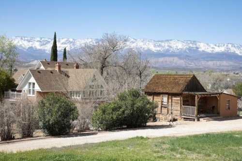 A scenic view of two houses, one modern and one rustic, with snow-capped mountains in the background and clear blue skies.