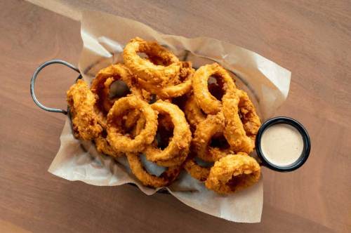 A basket of crispy fried onion rings served with a small cup of dipping sauce.