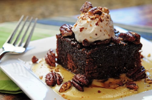 A rich chocolate dessert topped with whipped cream and pecans, served on a plate with a drizzle of sauce.
