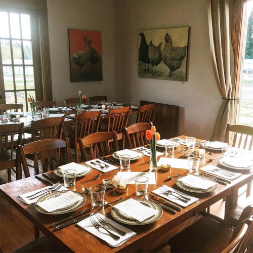 A cozy dining room set for a meal, featuring wooden tables, chairs, and chicken-themed artwork on the walls.