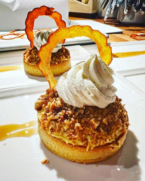 A dessert featuring a nutty crust, topped with whipped cream and a decorative slice of dried fruit.