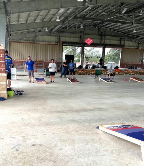 A group of people playing cornhole in a spacious indoor venue with decorations and a stage in the background.