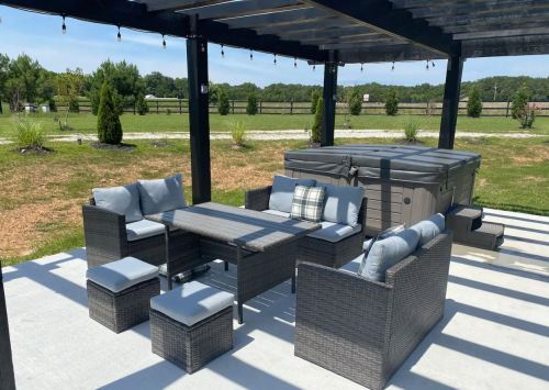 A patio area with a seating set, table, and hot tub, surrounded by greenery and a clear blue sky.