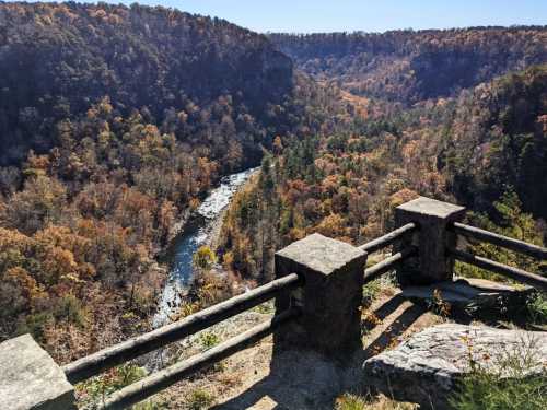 A scenic overlook of a river winding through autumn-colored hills and trees, with stone railings in the foreground.