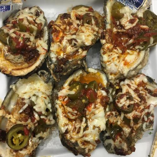 Baked oysters topped with cheese, jalapeños, and a spicy sauce, served on a bed of ice.