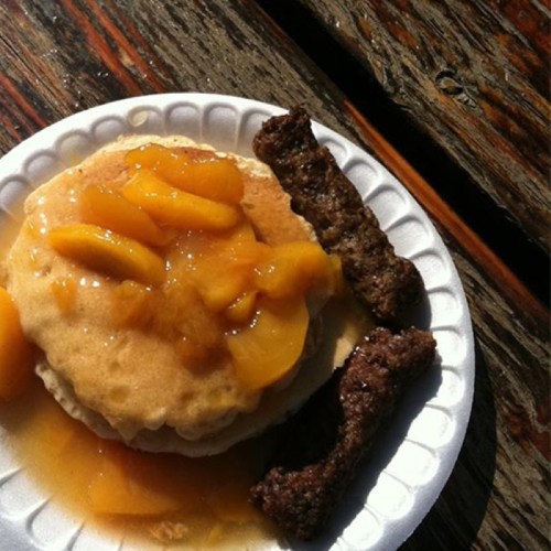 A plate with a pancake topped with peach slices and syrup, accompanied by two sausage links.