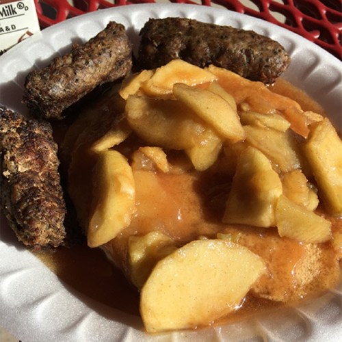 A plate with sausage links and a serving of warm apple slices topped with cinnamon sauce.