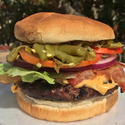 A delicious burger with a beef patty, cheese, lettuce, tomato, onion, pickles, and jalapeños on a toasted bun.