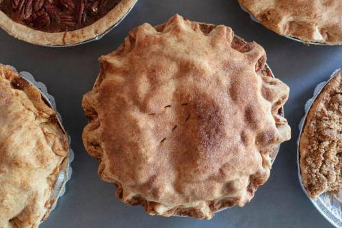 A freshly baked pie with a golden-brown crust, surrounded by other assorted pies on a gray surface.