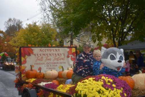 A woman and child in a wolf costume on a float decorated with pumpkins and flowers at a fall festival parade.