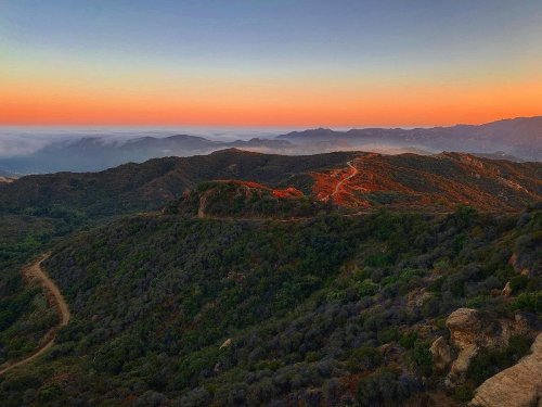 A scenic view of rolling hills at sunset, with vibrant orange and blue skies above a misty valley.