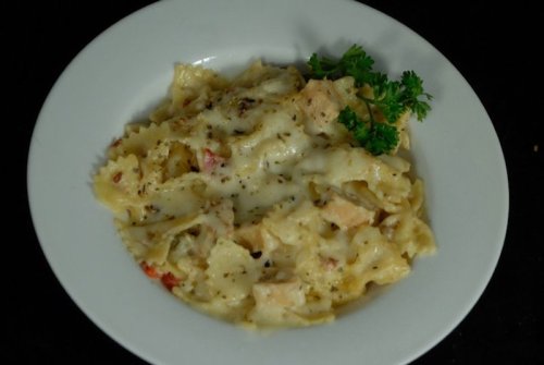 A bowl of creamy pasta with chicken, herbs, and cheese, garnished with a sprig of parsley.