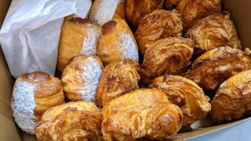 A box filled with various pastries, including flaky croissants and sweet rolls, some dusted with powdered sugar.