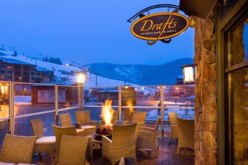 Outdoor seating area of Drafts Sports Bar & Grill, featuring a fire pit and snowy mountain backdrop at dusk.