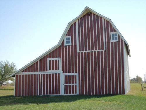 A red and white striped barn stands on a grassy field under a clear blue sky.