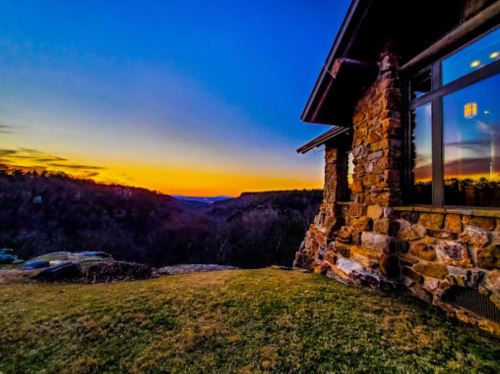 A stone house at sunset, overlooking a valley with vibrant orange and blue skies.