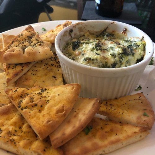 A plate of crispy flatbreads served with a creamy spinach dip in a white ramekin.