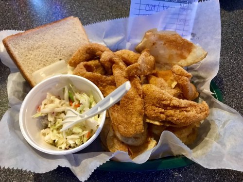 A plate of fried fish fillets with coleslaw and a slice of bread, served in a basket lined with paper.