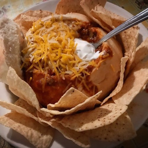A bowl of chili topped with cheese and sour cream, surrounded by tortilla chips.