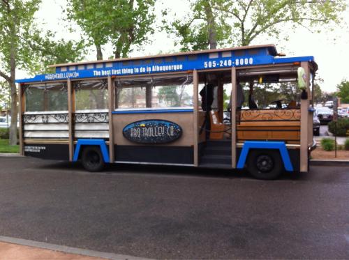 A colorful trolley bus parked on a street, featuring decorative designs and a sign promoting tours in Albuquerque.