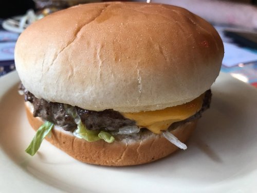 A close-up of a cheeseburger with lettuce, melted cheese, and a soft bun on a plate.