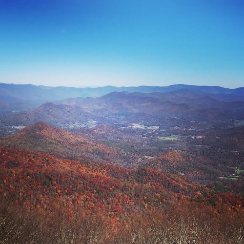 A panoramic view of mountains covered in vibrant autumn foliage under a clear blue sky.
