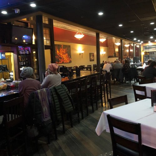 A cozy restaurant interior with a long bar, tables, and patrons enjoying their meals in a warm atmosphere.
