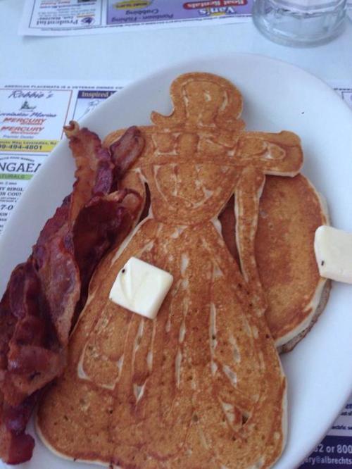 A plate with pancakes shaped like a dress, accompanied by bacon and butter.