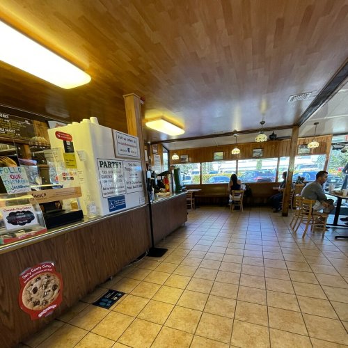 Interior of a cozy café with wooden decor, a counter, and customers seated at tables by the windows.