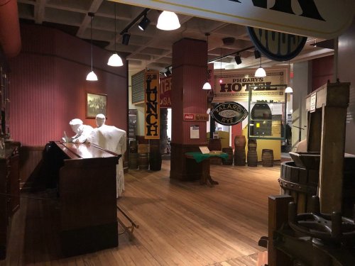 A vintage museum interior featuring mannequins, wooden barrels, and historical signage in warm lighting.