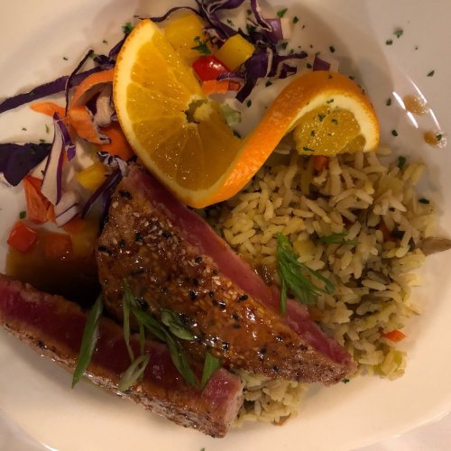 A plate featuring seared tuna, rice, colorful vegetables, and orange slices, garnished with herbs.