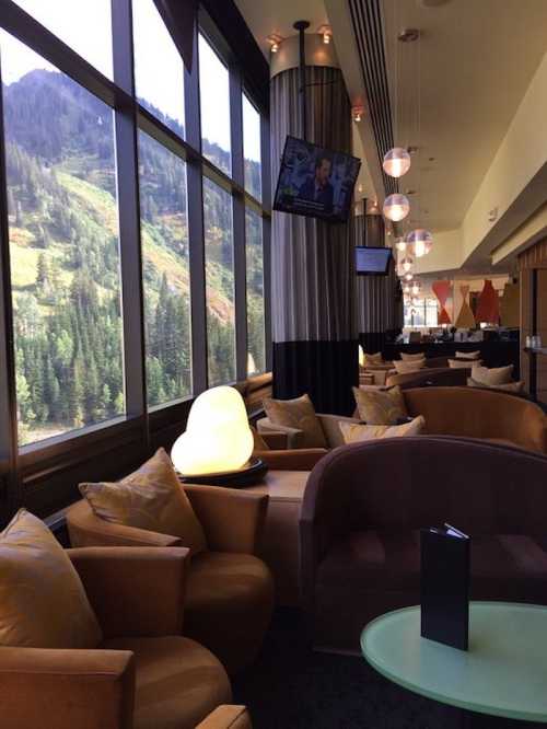 A cozy lounge with modern seating, large windows showcasing a mountain view, and a TV displaying news.