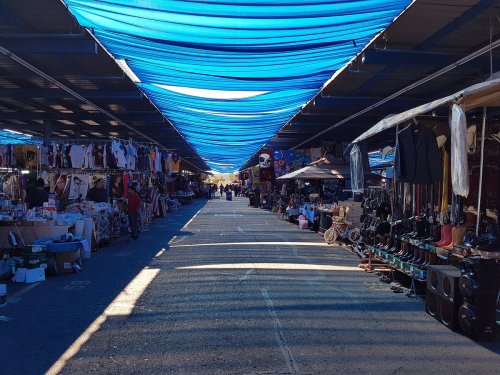 A bustling market with colorful canopies, lined with stalls selling clothes and various goods under a blue sky.