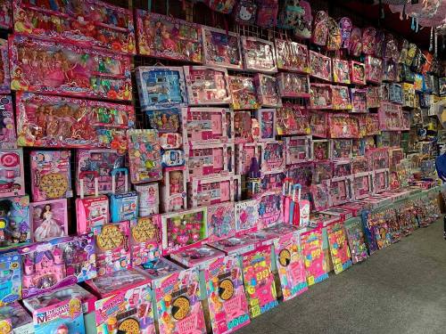 A colorful display of various toys and dolls, predominantly in pink packaging, arranged on shelves.