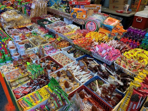 A colorful display of various candies and snacks in baskets at a market stall.