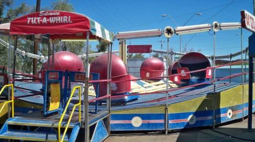 A colorful Tilt-A-Whirl ride at an amusement park, featuring red and blue seats and a vibrant canopy.