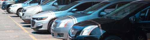 A row of parked cars in a parking lot, featuring various makes and models in different colors.