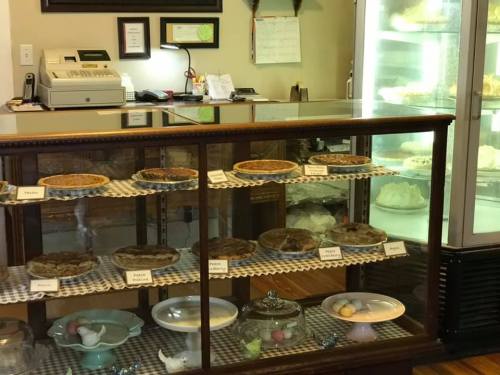 A display case filled with various pies, including pecan and apple, in a cozy bakery setting.