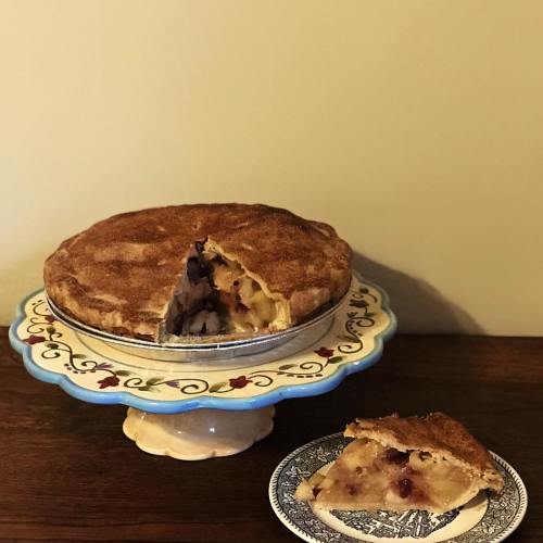 A freshly baked pie on a decorative stand, with a slice cut out and placed on a plate beside it.